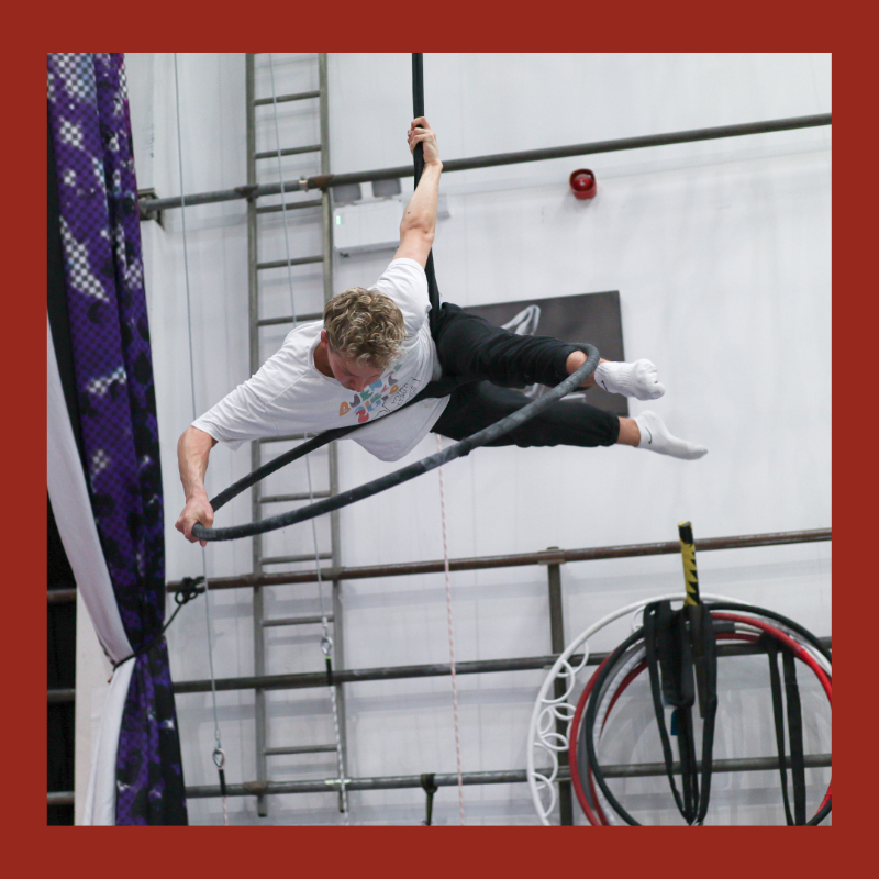 Aerial hoop student performs a move on the top of the equipment