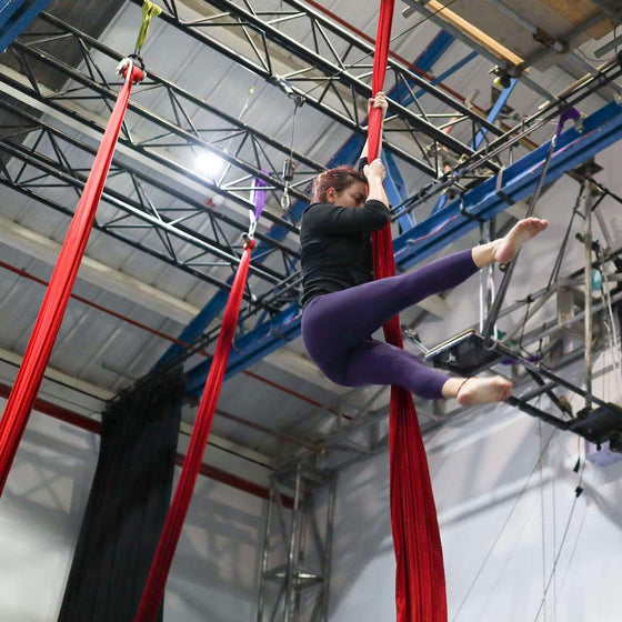 Aerial silks student holds a straddle position whilst hanging from the silks