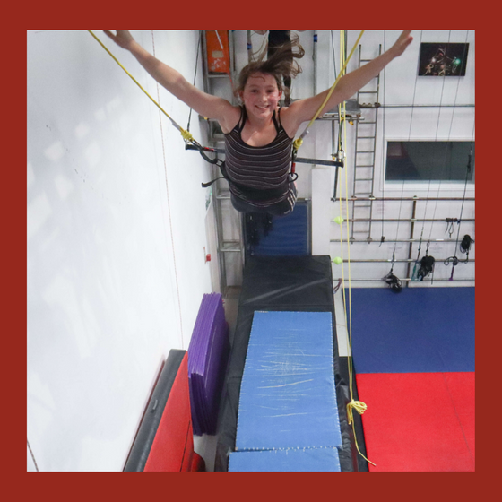 Flying trapeze student performs a dismount and smiles at the camera