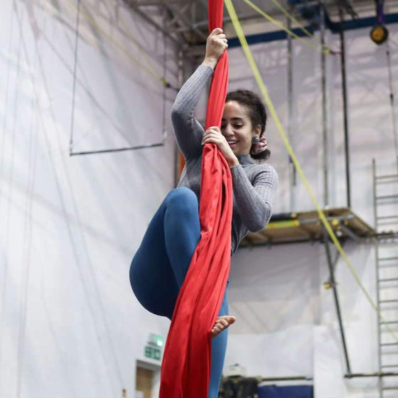 Aerial silks student prepares to climb the silk, smiliing