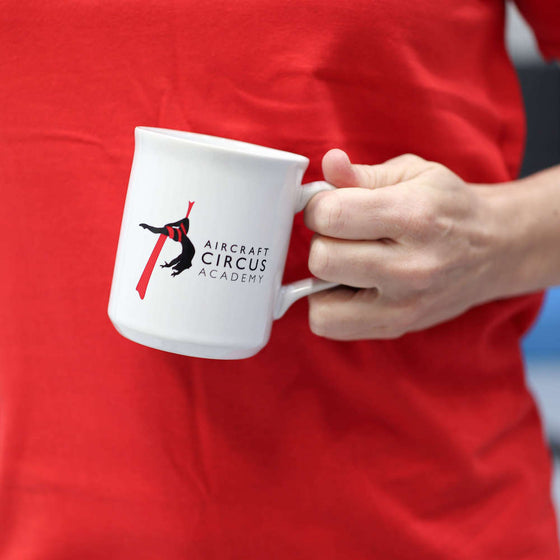 A white mug with the AirCraft Circus Academy logo on it