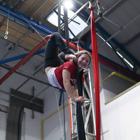 Youth student performs a backbend in the silks, smiling at the camera