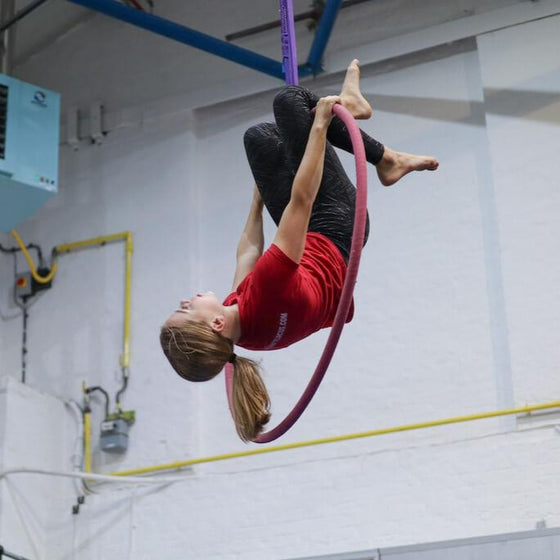 Youth student hangs by her knees on the top of an aerial hoop